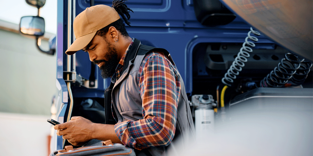 Truck driver sitting on the back of his trailer looking at his phone.